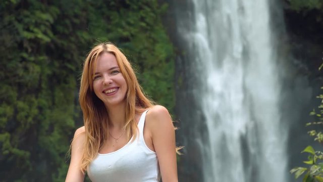 Young caucasian happy woman smiling and laughing in front of Bajing Waterfall on sunny day in Pekalongan,Indonesia
