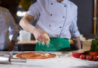 chef sprinkling cheese over fresh pizza dough