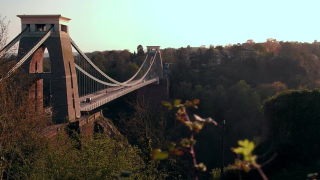 Camera slides over hedgerow with the Clifton Suspension Bridge behind. Shot during a spring sunset