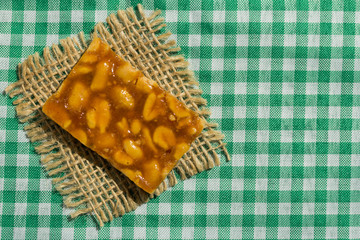 Candy with peanut: Pe de Moleque in Brazil and Chikki in India. Sweet food of Festa Junina, a typical brazilian party. Snack on green plaid table and jute.