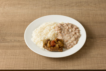 White rice, pinto beans and meat with sauce. White dish on wooden table.