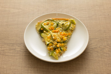 Slice of pizza: Toppings are zucchini, corn kernels and mozzarella cheese. Wooden table.