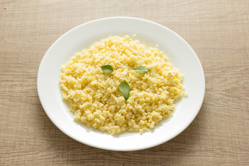 Cooked Millet cereal grain on white plate and wooden table.