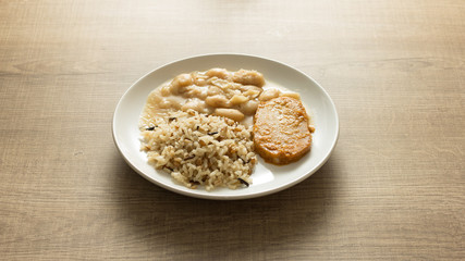 Pork chop, Brown rice and white beans. White dish on wooden table.