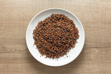 Cooked Red and Black Quinoa mixed. Meal on white dish and wooden table. Overhead, flat lay of meal.