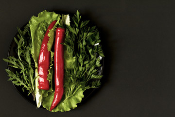 Chili pepper with greens  on a plate on a black background.