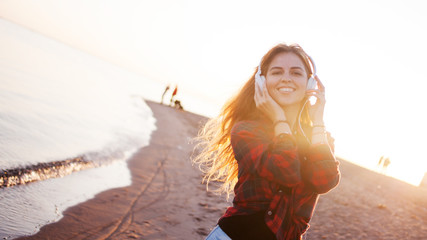 Happy attractive red-haired girl is enjoying favorite music on walk. Beautiful young woman in shirt uses headphones