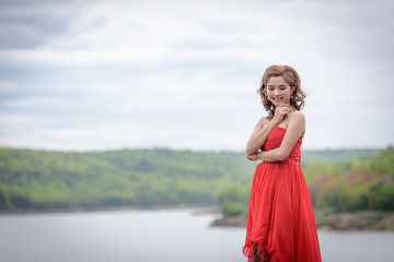 Fototapeta na wymiar Beautiful woman wear red evening dress over mountains and rivers background.