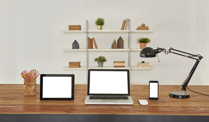 Laptop tablet and smartphone on the wood table in the office style with bookcase background.