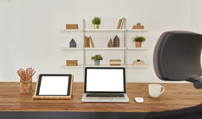 modern workplace wooden table with laptop tablet. Decorative office background with bookcase.