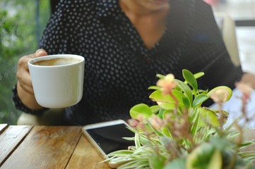 Woman are reading the document.The right hand holds a glass of white coffee ready to drink.And there are mobile phones placed next to the ornamental trees on wooden table.
