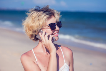 Young happy woman talking on mobile phone on a beach with sea background