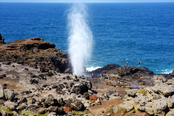 Tourists admiring the Nakalele blowhole on the Maui coastline. A jet of water and air is violently...