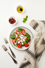 Tomatoes, spinach leaves, red onions and feta cheese salad on a light ceramic plate. Selective focus. Top view.