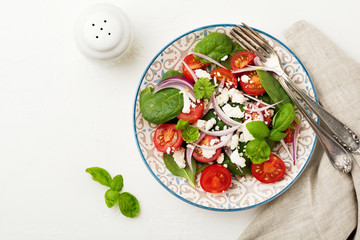 Tomatoes, spinach leaves, red onions and feta cheese salad on a light ceramic plate. Selective focus. Top view.