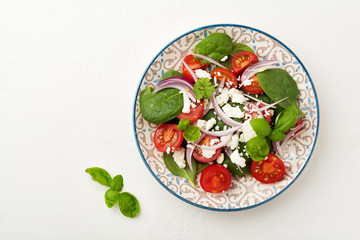 Tomatoes, spinach leaves, red onions and feta cheese salad on a light ceramic plate. Selective focus. Top view.