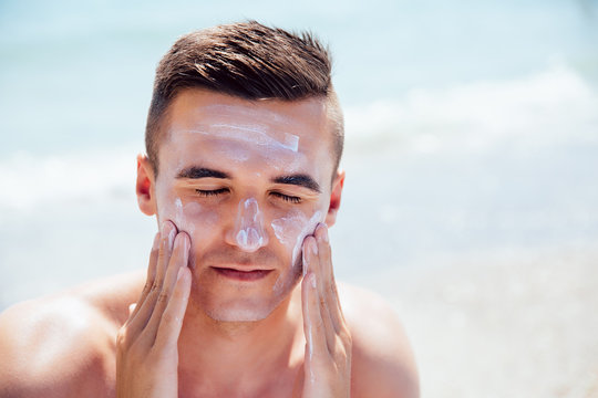 Attractive Man Putting Tanning Cream On His Face, Closing His Eyes, Takes A Sunbath On The Beach. Healthcare.