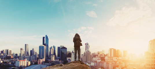 Plakat a man with backpack standing on the mountain enjoying beautiful sunrise in the city