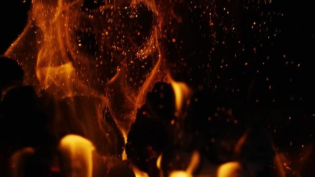 Closeup slow motion shot of fire sparks moving on dark at black background coming from brightly burning warm