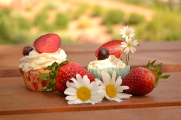 Sweet creamy fruit cakes with strawberries and flowers on wooden table decoration