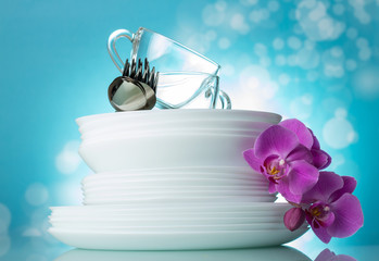 Stack of clean plates, cups, spoons and forks on light blue