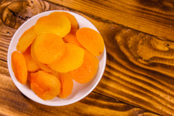 Ceramic plate with dried apricots on wooden table. Top view