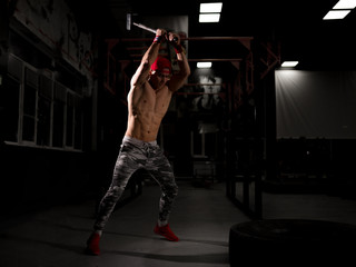 A young sportsman in a red cap in the gym. Do exercises with a hammer. Crossfit training in the gym.