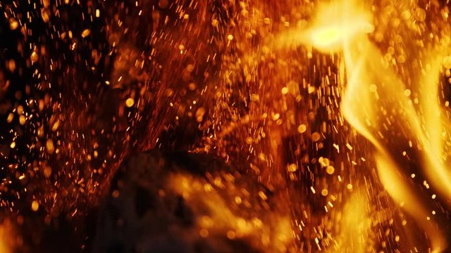 Closeup slow motion shot of fire sparks moving on dark at black background coming from brightly burning warm