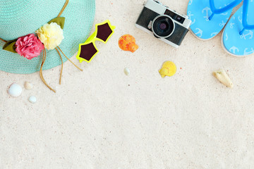 Beach background.  Top view of beach sand with straw hat, sunglasses, shells, camera, slippers and coral.  Summer background concept.