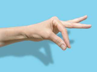 Female hand isolated on blue background with shadow. The thumb and forefinger are assembled into a pinch. communication symbols and gestures. Isolated object