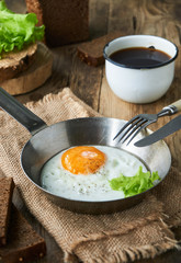 Fried egg in a frying pan with lettuce on a wooden table     