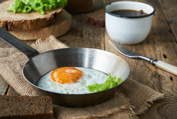 Fried egg in a frying pan with lettuce on a wooden table     