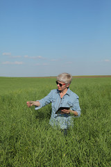 Naklejka na ściany i meble Female agronomist or farmer examining green canola field using tablet, rapeseed plant in spring