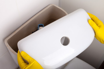 Plumber repairing toilet cistern at water closet, closeup