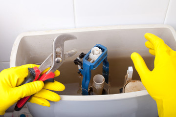 Plumber repairing toilet cistern at water closet, closeup