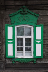 The window with the wooden carved architrave in the old wooden house in the old Russian town.