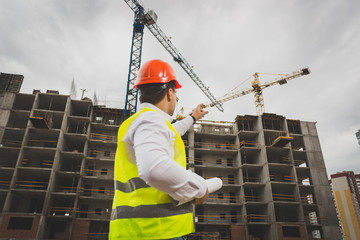 Toned image of male construction worker pointing at working cranes on building