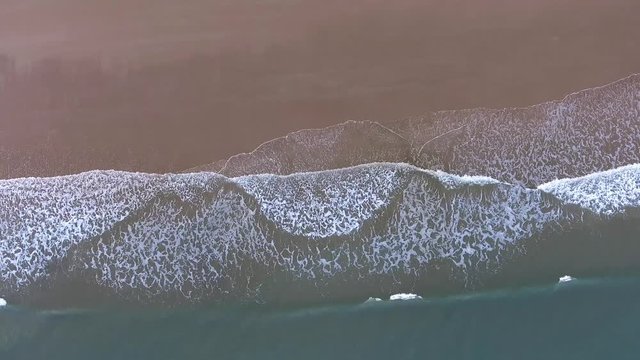 Vertical downward aerial view of waves breaking onto the sandy beach of Oxwich Bay on the Gower peninsula, Swansea, South Wales, UK