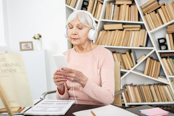 Listen carefully. Concentrated mature woman listening to audio and using phone