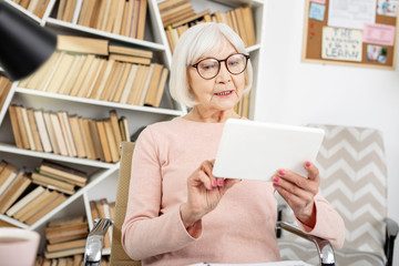 Educational courses. Musing senior woman using tablet while sitting in chair