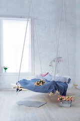 White loft interior in classic scandinavian style. Hanging bed suspended from the ceiling. Cozy large gray plaid, spring flowers lie on the bed, stand in a basket on the floor. Trendy room design