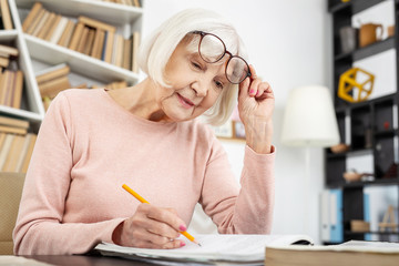 Effective study. Low angle of nice senior woman putting fingers on glasses while learning
