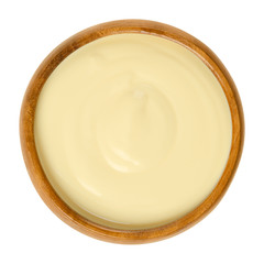 Sauce Hollandaise in wooden bowl. Also Dutch sauce. Emulsion of egg yolk, butter, water and lemon juice. Eaten with steamed vegetables or Eggs Benedict. Macro food photo close up from above over white
