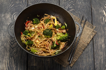 In pan-wok noodles with meat and broccoli, chopsticks on wooden table