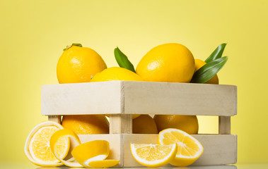 Box of lemons next to slices of citrus fruit and peel, on bright yellow
