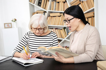 Dictation translation. Asian tutor carrying book while senior woman writing down