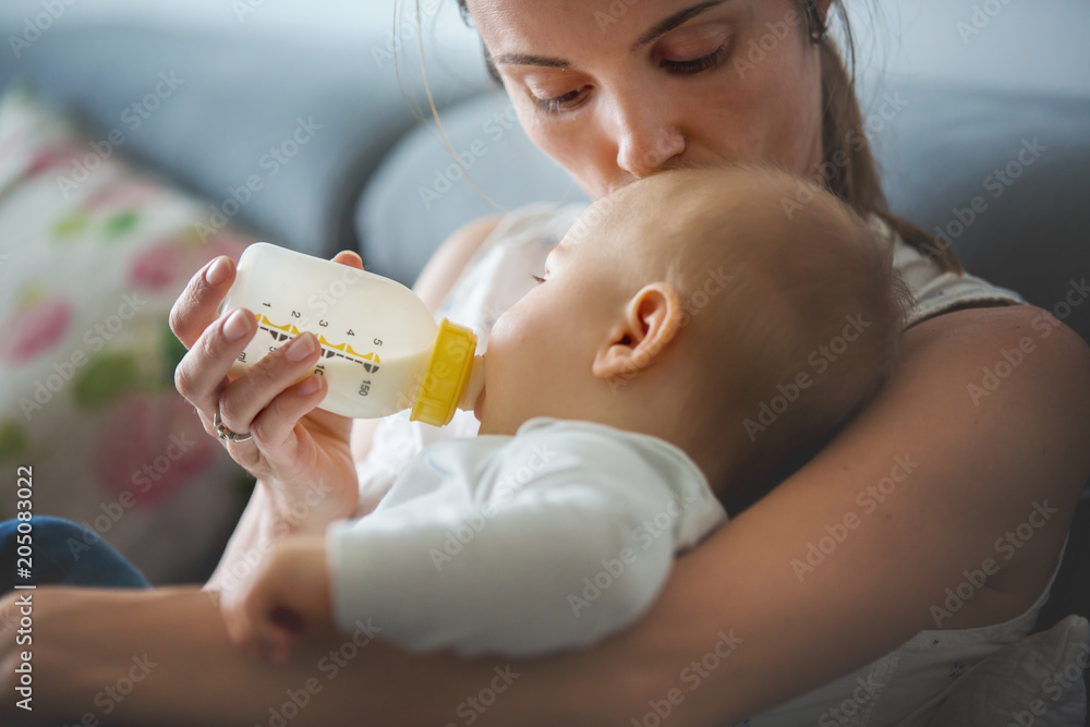 Canvas Prints Mother, feeding her baby boy from bottle, sitting on the couch at home