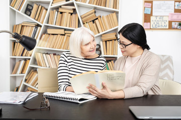 Full explanation. Appealing tutor carrying book while senior woman asking question