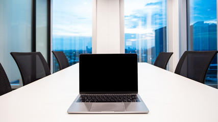 modern laptop on foreground at meeting room with large windows, outside building, city, tower view, soft focus