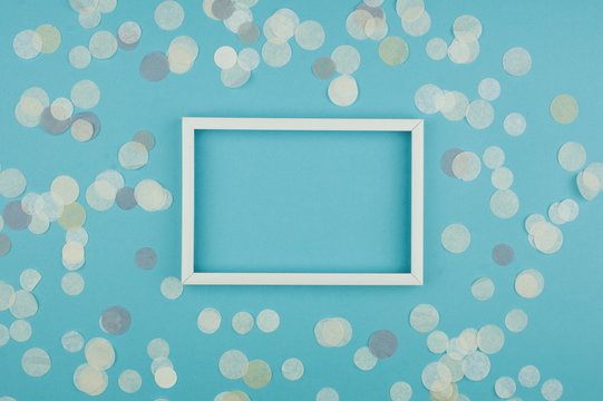 White frame and confetti on blue background. Top view, flat lay. Mockup for party or birthday invitation.